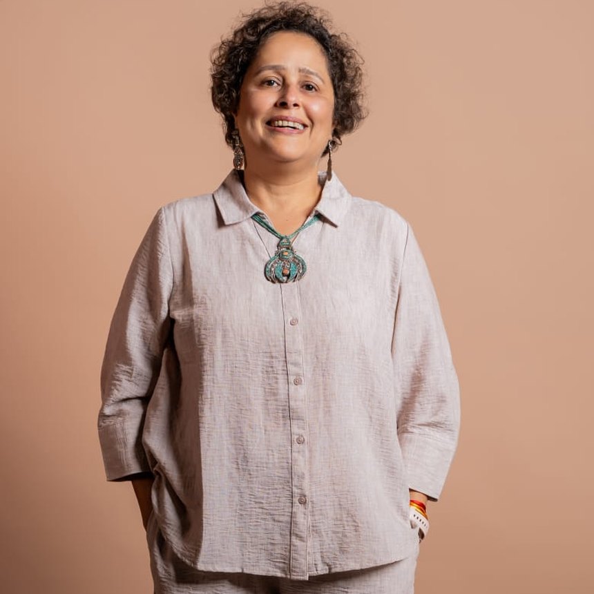Chelna Lekhi, smiling, in a linen shirt against a warm studio backdrop