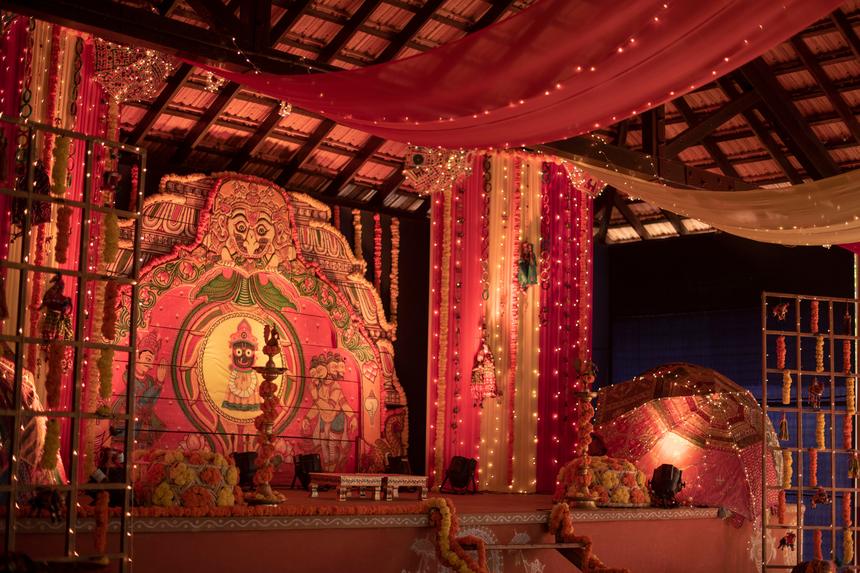 A red and gold wedding mandap lit under a timber pavilion
